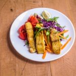 A plate of baked fish served over a fresh garden salad