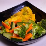 A plate of steamed fish served with an array of colorful steamed vegetables